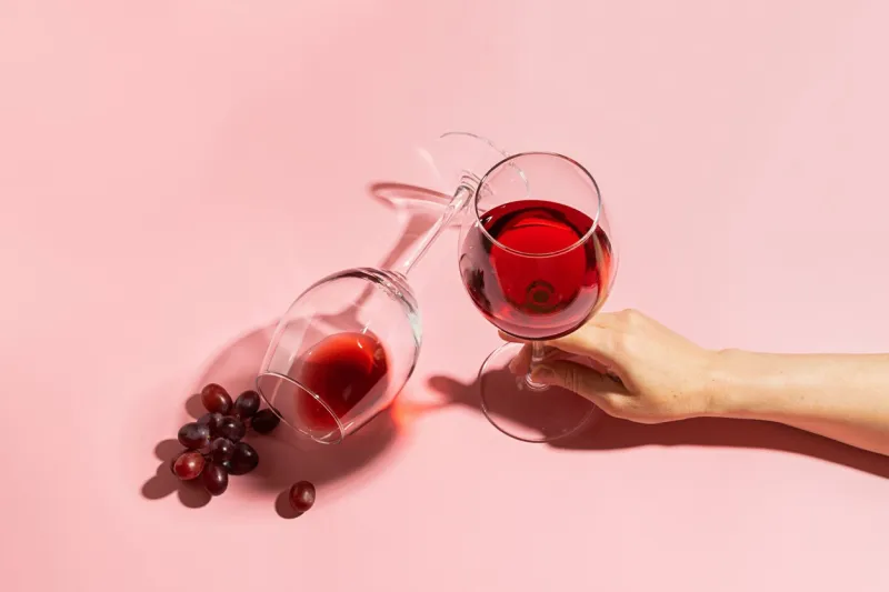 female hand holding a glass with red wine and a bunch of grapes on a gentle pink background selective focus copy space minimalism top view flat layout