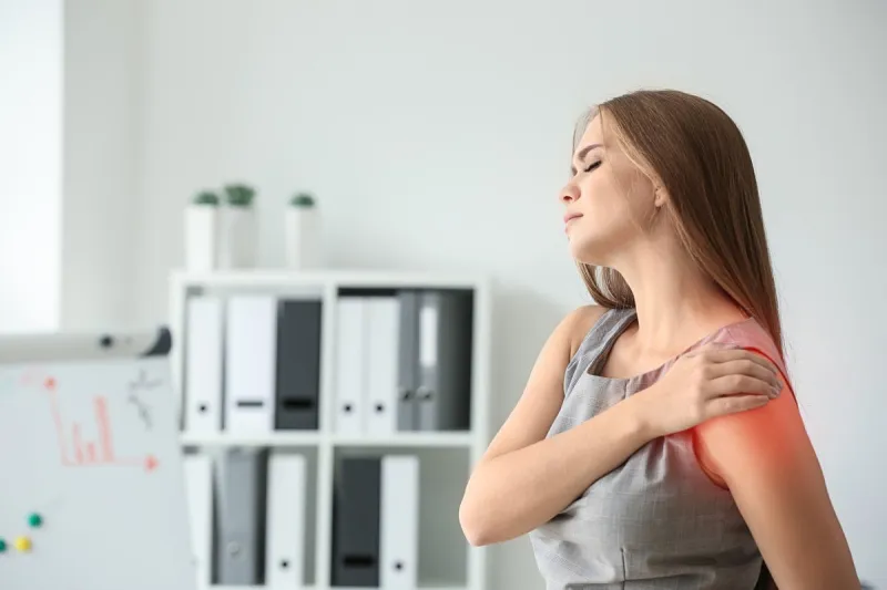 young woman suffering from pain in shoulder at workplace