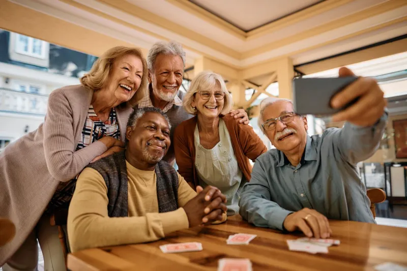 multiracial group of happy senior people taking selfie with cell phone in nursing home