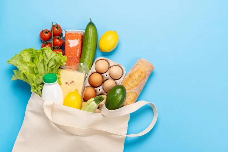 shopping bag full of healthy food on blue background flat lay with copy space