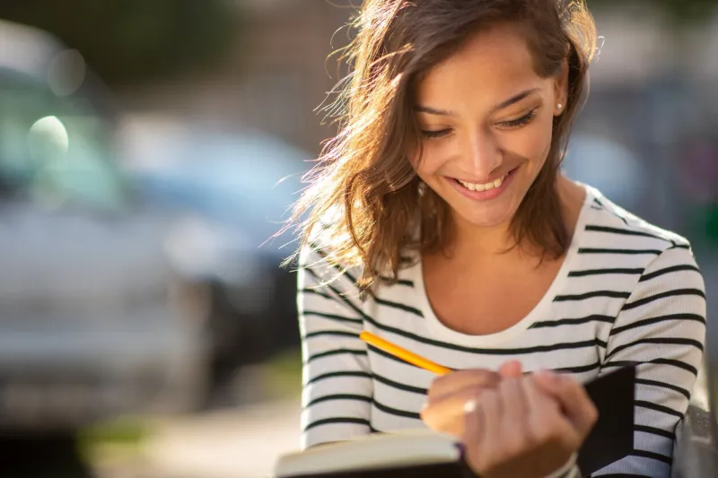 close up portrait smiling young woman writing notes in book