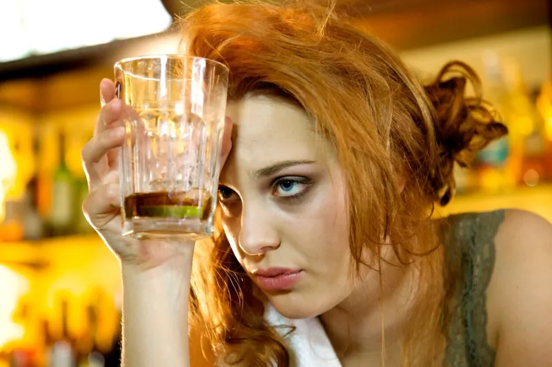 young woman with a hangover holding her almost empty cocktail glass