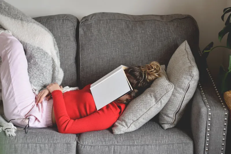 young girl lying on a couch napping with a book covering her face
