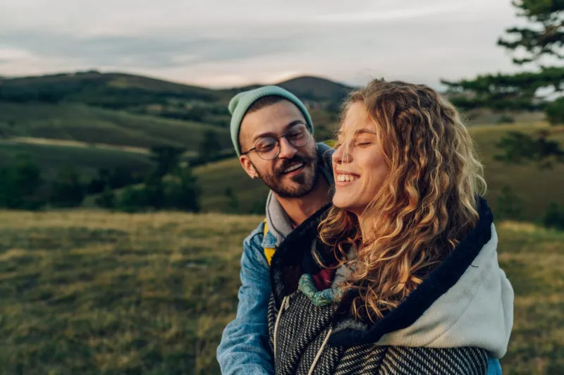 happy couple in love embracing and following trail along grassy mountain ridge and having fun together while walking in the nature healthy lifestyle and romantic getaway focus on a smiling woman