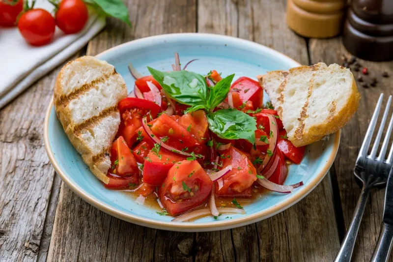 tomato salad with red onion and bread on wooden table
