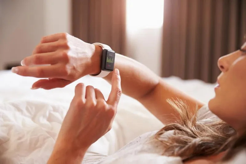 femme couchée dans son lit tout en vérifiant l'application de remise en forme sur une montre intelligente