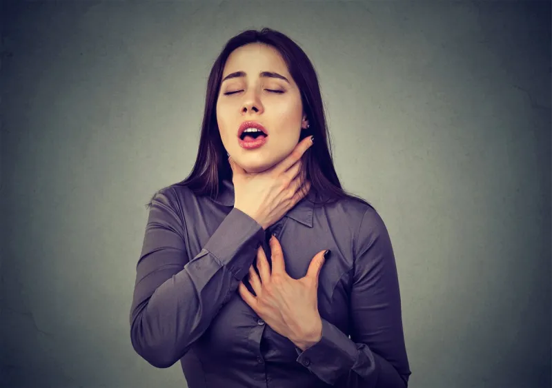 young woman having asthma attack or choking can't breath suffering from respiration problems isolated on gray background