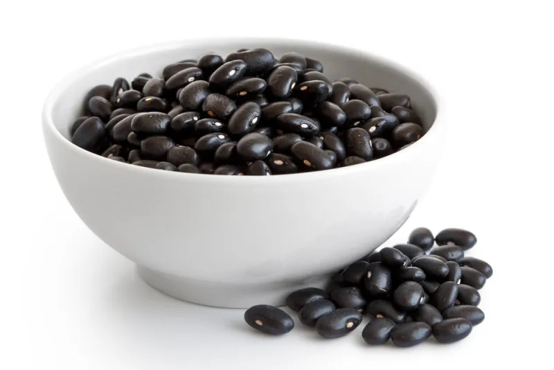 black beans in white ceramic bowl isolated on white spilled beans