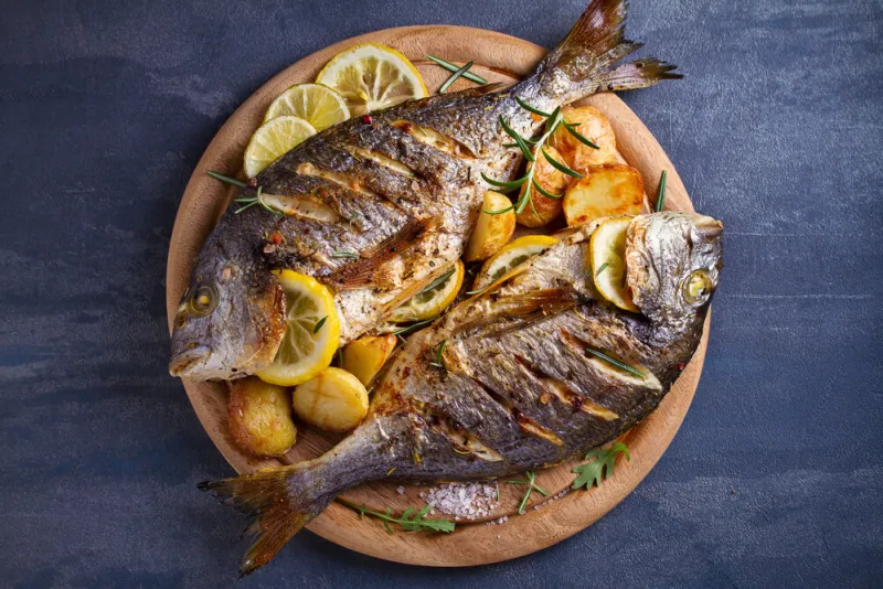 roasted fish and potatoes, served on wooden tray overhead, horizontal - image