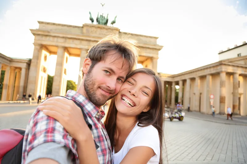 happy couple selfie selfportrait in front of brandenburg gate or brandenburger tor, berlin, germany beautiful young multiracial travel couple having fun on europe vacation asian woman, caucasian man