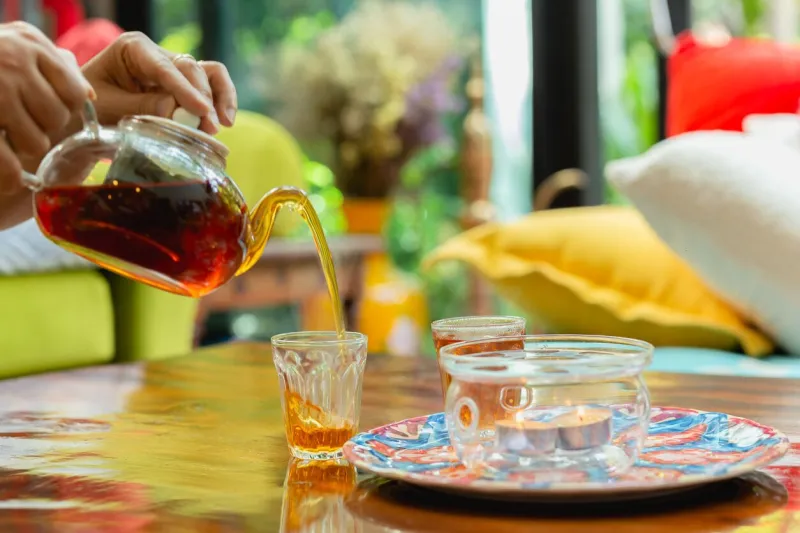 woman pouring tea into a cup from tea pot on wooden table