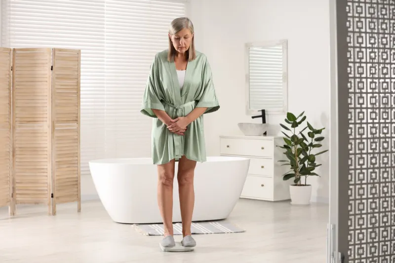 menopause, weight gain concerned woman standing on floor scales in bathroom