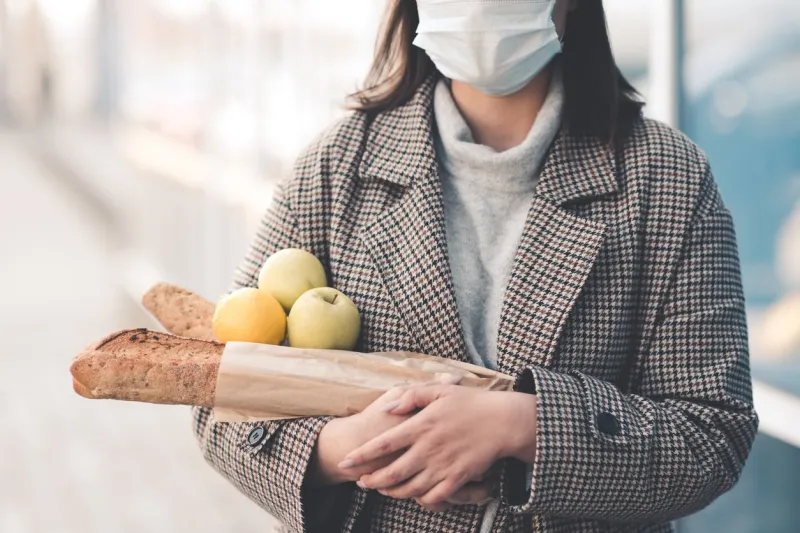 young woman holding food walking on street wearing medical mask outdoors social distancing virus concept