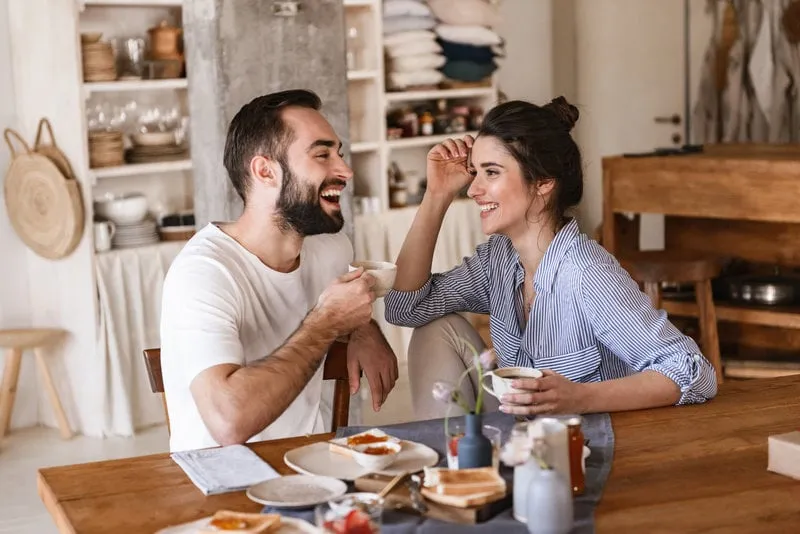 image of modern brunette couple man and woman 20s eating breakfast together while sitting at table at home