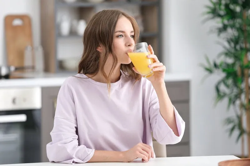 beautiful young woman drinking orange juice in kitchen