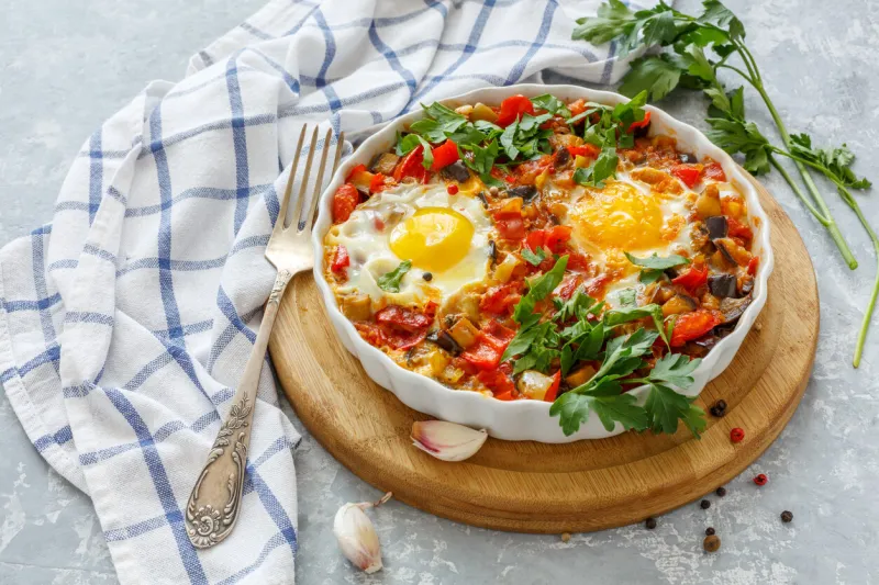 traditional israeli dish with vegetables in ceramic dishes on a serving board, linen cloth and fork