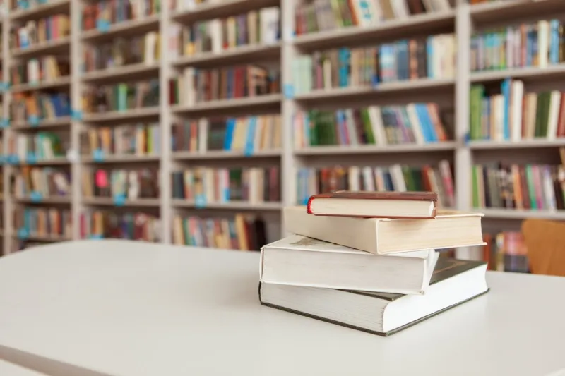 pile of books on the table at college library, stacked bookshelves on background book stack at library room