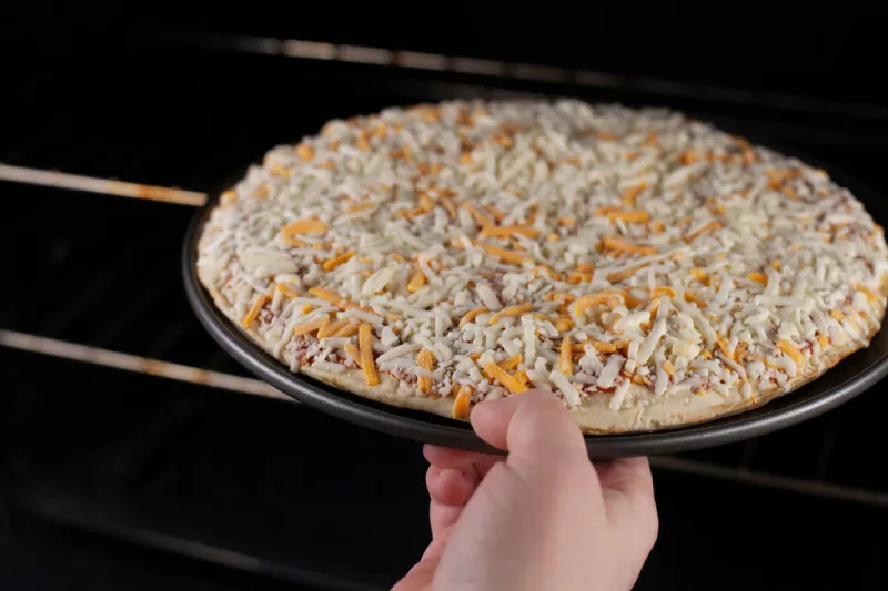 putting frozen cheese pizza into the oven to bake