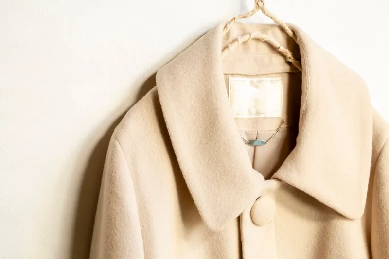 beige wool coat hanging on clothes hanger on white backgroundclose up