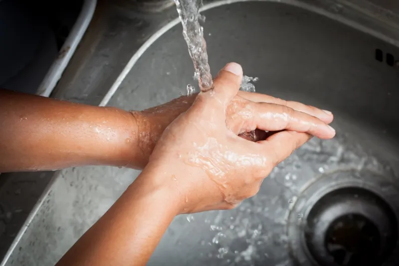woman washing her hands under running water in kitchen room