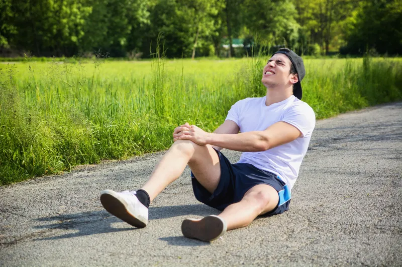 beau jeune homme blessé lors de la course et le jogging sur la route dans le pays dans une journée ensoleillée, portant une chemise blanche et une casquette de baseball
