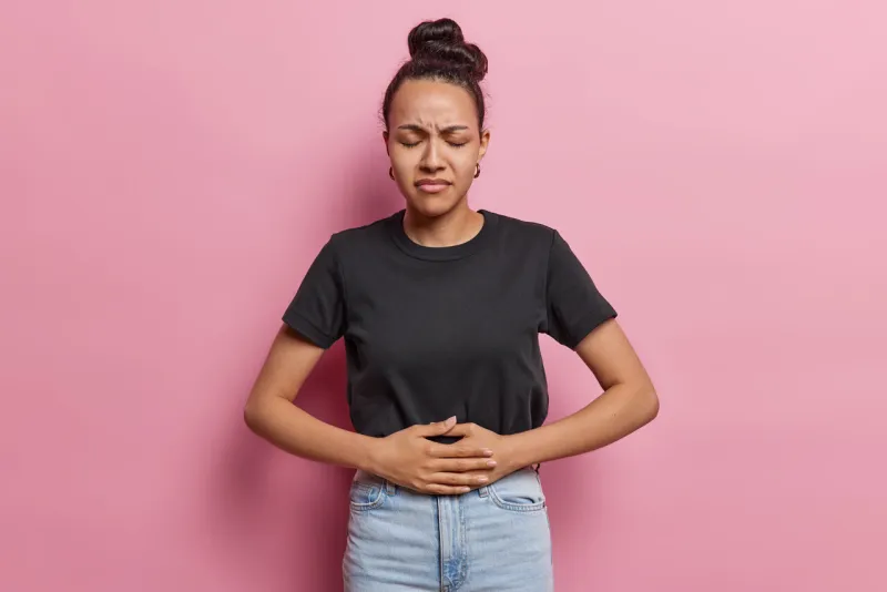 upset sad worried latin woman has stomach ache disorder feels unwell suffers from indigestion feels abdominal pain or cramps dressed casually isolated over pink background health problems concept