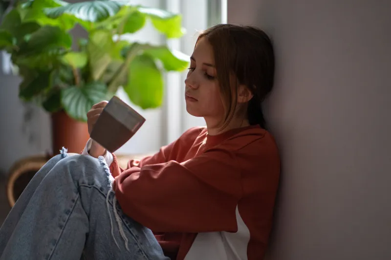 frustrated sad teenage girl sitting on floor with cup devastated thinking about trouble, broken heart young woman have bad mood due to hormones in period depressive thoughts from problems at school