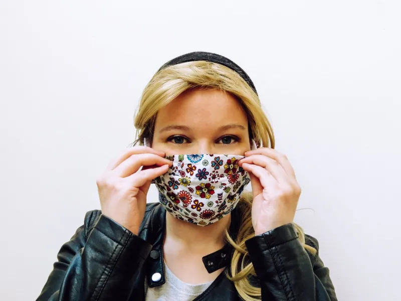 young blonde caucasian woman wearing colorful face mask made of fabric isolated in front of white background
