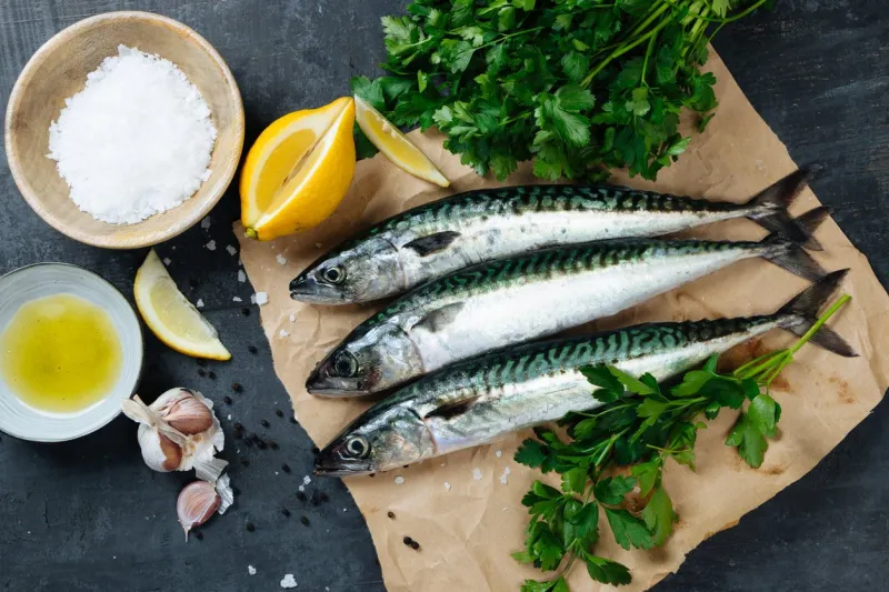 fresh mackerel fish on paper with lemon, salt, olive oil, garlic, parsley and pepper top view