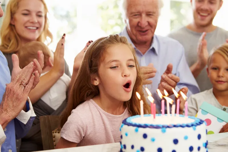 girl blows out birthday cake candles at family party