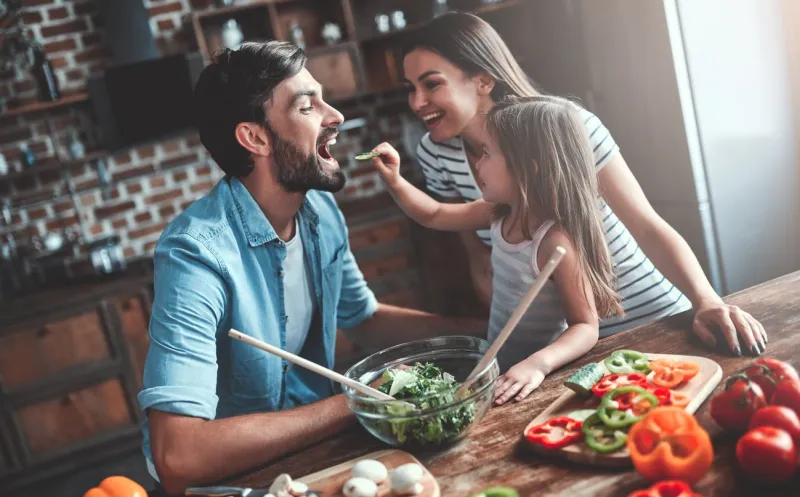 mom, dad and daughter are cooking on kitchen happy family concept handsome man, attractive young woman and their cute little daughter are making salad together healthy lifestyle