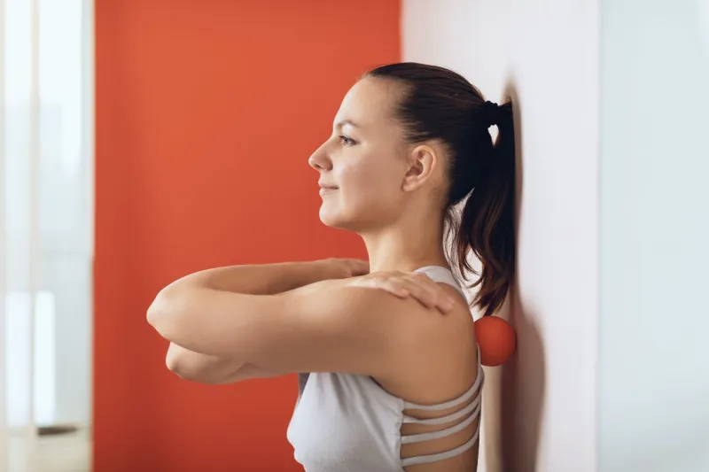 beautiful woman performs myofascial release of hyper-flexible muscles of the back with a massage ball near the wall the concept of back fatigue prevention and self-massage