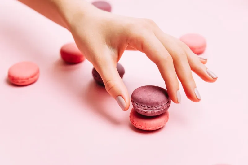beautiful female hands with trendy manicure holding pink macaroon cake top view, flat lay copyspace for your text