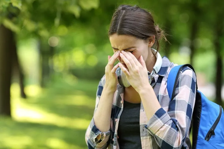 student suffering allergy symptoms scratching eyes in a park