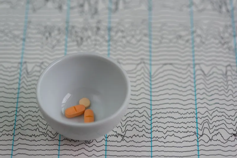 close-up image of three pills for antiseizure in a white dish placed on top of an eeg (electroencephalogram) graph