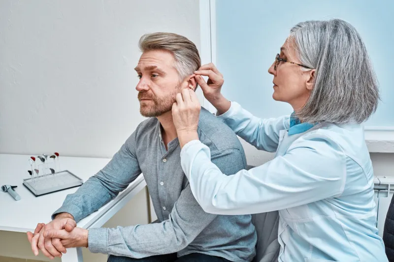 experienced female doctor fitting intra-the-ear hearing aid into patient's ear while consultation in audiology clinic ite and itc hearing aids