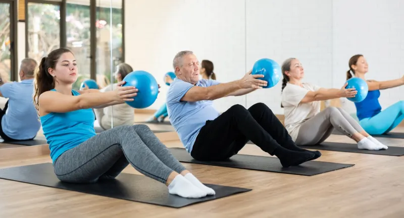 group of sporty people of different ages doing sit-ups with bender balls to strengthen abdominal muscles during pilates class in fitness studio