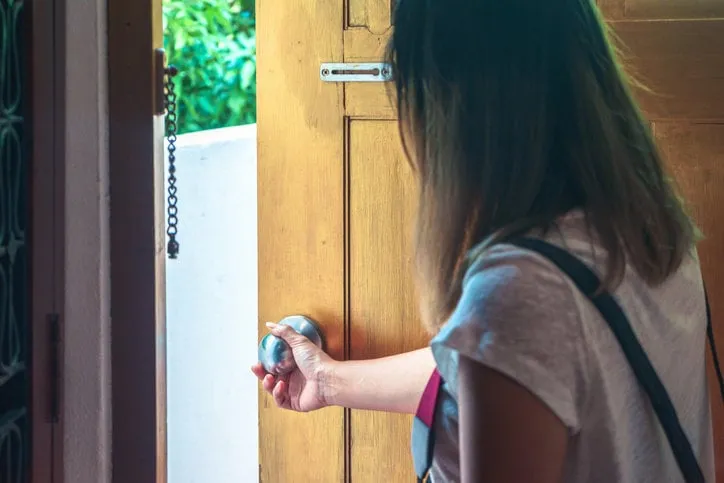 asian woman grabbing door knob opening brown wooden door