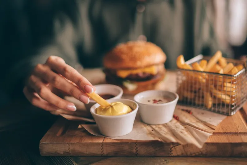 french fries and ketchup in basket with flare light fast food, people and eating concept close up of hand with dipping french fries into ketchup bowl on wooden table selective focus