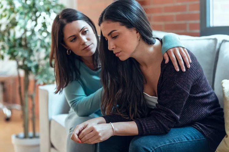 shot of pretty young woman supporting and comforting her sad friend while sitting on the sofa at home