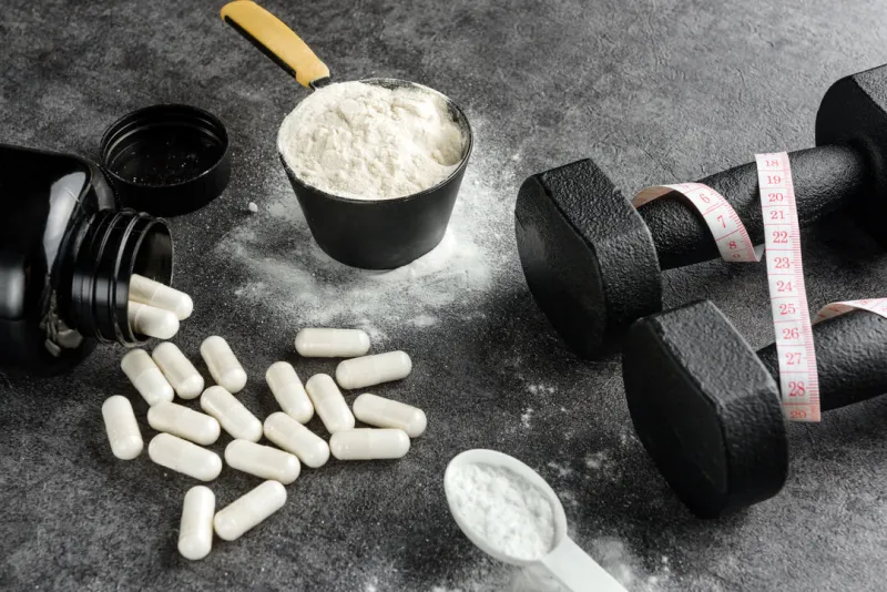 protein scoop, creatine capsules and dumbbells with measuring tape the concept of the usefulness of sports nutrition