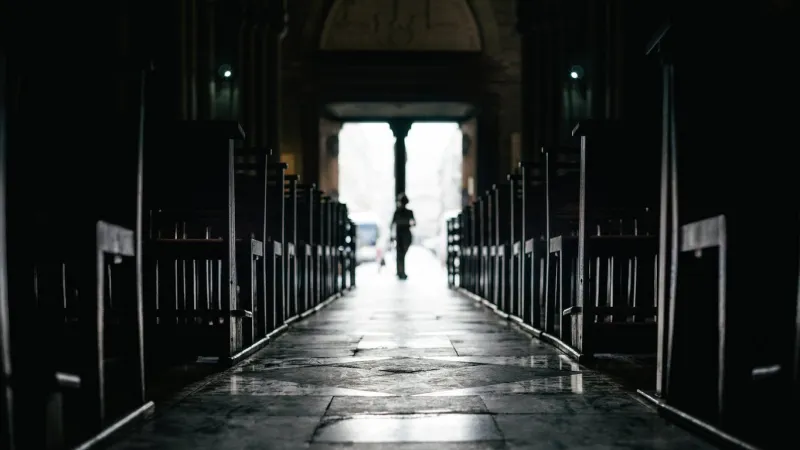 rows of bench inside a silent church with passerby moving in from exit