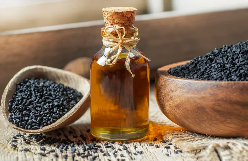 glass bottle of black cumin seeds essential oil , nigella sativa in spoon on wooden background organic herbal medicine for many diseases, black cumin