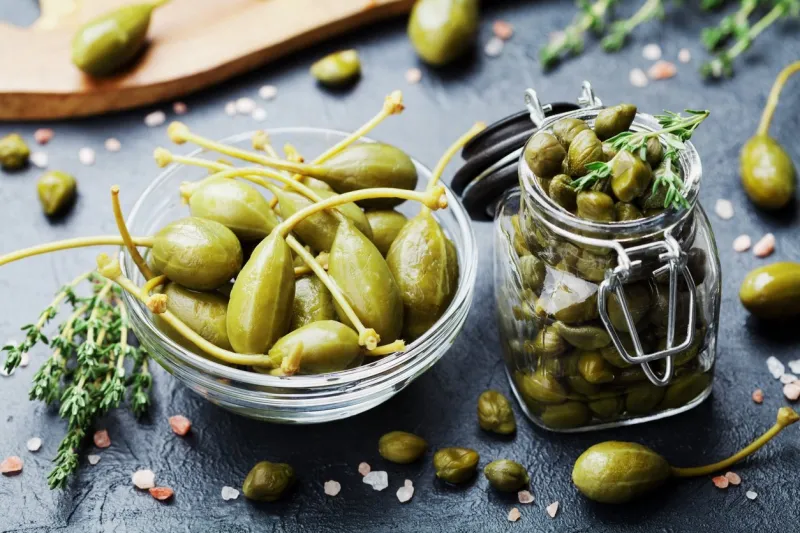 mixed capers in jar and bowl on black stone kitchen table
