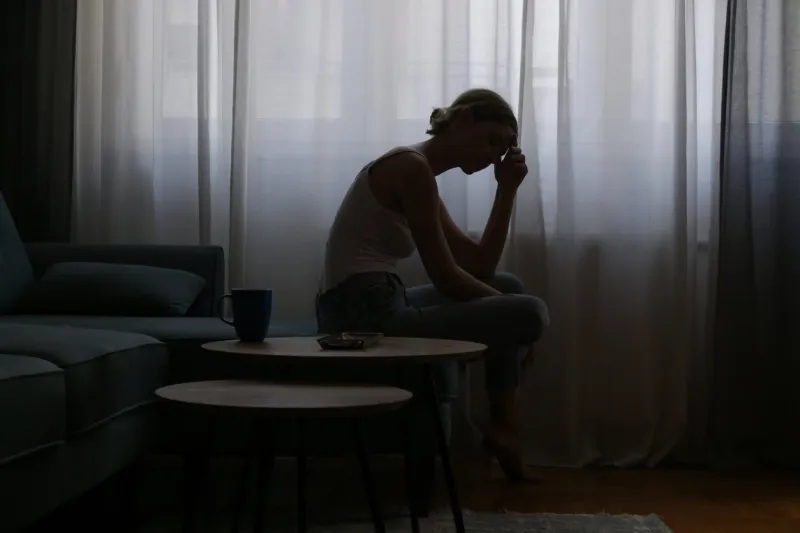 young depressed woman sitting on the sofa next to the window