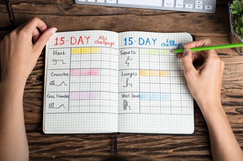 close-up of a human hand making exercise plan on notebook over wooden desk