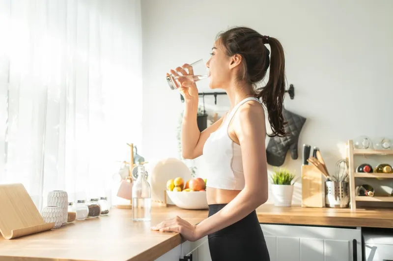 asian beautiful woman in sportswear drink water after exercise at home young thirsty active sport girl takes a sips of clean mineral natural in cup after workout for health care in kitchen in house
