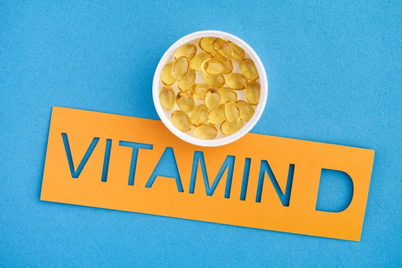 the word vitamin d with a small cup of vitamin d3 capsules on it close up