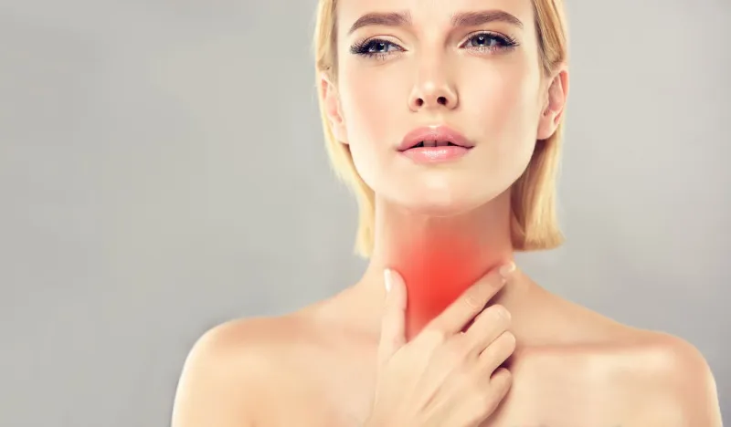 young, attractive woman is touching the neck with expression of sharp pain on the face symbolic image of sore throat, any type of inflammation, endocrinology problems, thyroid gland diseases