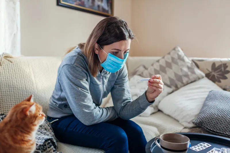 ill infected woman checking thermometer having fever girl wearing protective mask while having cold, flu taking pills at home healthcare